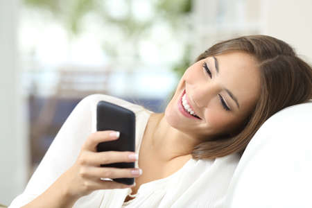 Happy girl texting on a mobile phone resting on a couch at home