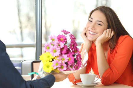 Couple dating and boyfriend giving a bouquet of flowers to his candid girlfriend in a coffee shop Фото со стока