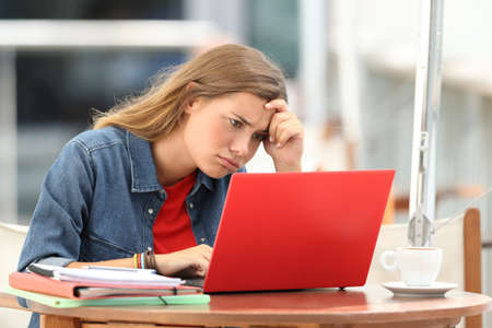 Single frustrated student trying to understand on line tutorials in a laptop sitting in a restaurant