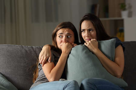 Scared friends listening noise at home in the night sitting on a couch in the living room at home Foto de archivo - 102851866