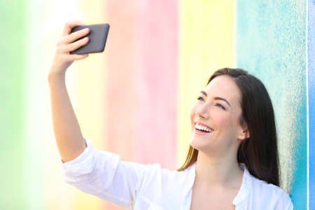 Happy woman taking selfies with smart phone in a colorful wall in the street