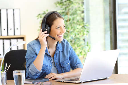 Happy tele operator woman attending call looking away at office Stock Photo