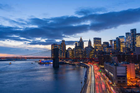 New york city skyline aerial view from manhattan bridge with skyscrapers background at dusk financial district of nyc with traffic light trails on fdr drive that runs along the east river