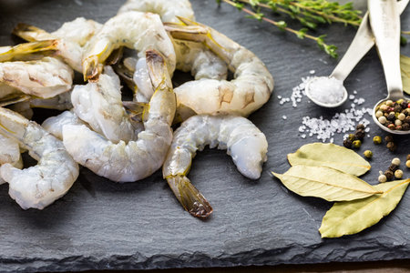 Raw peeled shrimp with tails with lemon on sutting board.