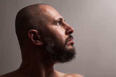 serious bald man with beard in profile on dark studio background