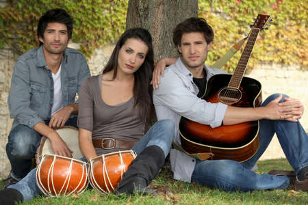 Woman beat guitar: three musicians at the foot of a tree