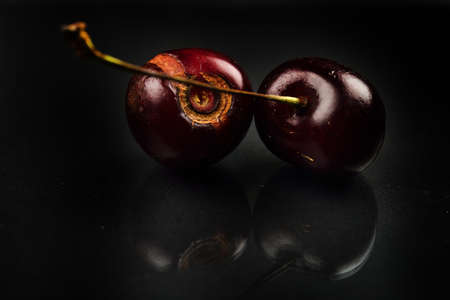 Close up of image of rotten red cherries fruit on reflective black background. selective focus. lights and shadows