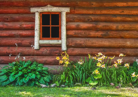 Wooden Facade Of A Rustic Decorative House With Garden Flowers Lilies Under The Window.