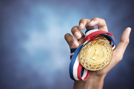 Hand holding up a gold medal as a winner in a competition Stock Photo