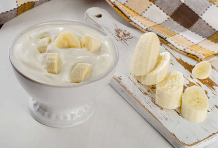 banana: Yogurt with banana in a white bowl on white wooden table.