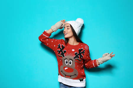 Young woman in christmas sweater and knitted hat on color background