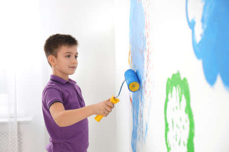 Little child painting wall with roller brush indoors