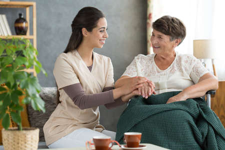 retirement home volunteer holding elder womans hand in gesture of support before rehabilitation stock photo