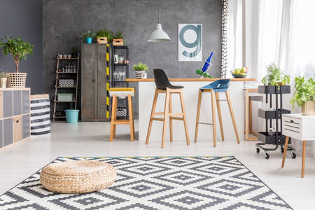 Pouf On Geometric Carpet In Spacious Dining Room With Bar Stools At Kitchen Island Against Concrete Pouf On Geometric Carpet In Spacious Dining Room With Bar Stools At Kitchen Island Against Concrete
