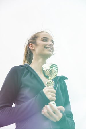 Happy sporty young woman holding gold trophy cup outdoor