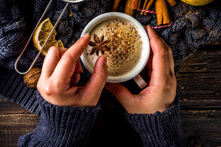 Boisson chaude sucrée d'automne, Chai Buttered Rum, Pumpkin Pie ou Pumpkin Spice Coffee Latte. Fond d'automne confortable. Fille tenir une tasse de latte traditionnelle dans les mains, sur fond de bois rustique