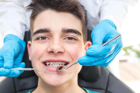 Dentysta z narzędziami w ustach młodego mężczyzny z ortodoncją