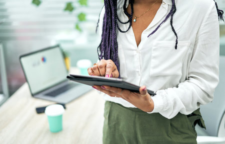 Primer plano de las manos de una mujer de negocios de pie en la oficina usando una tableta.