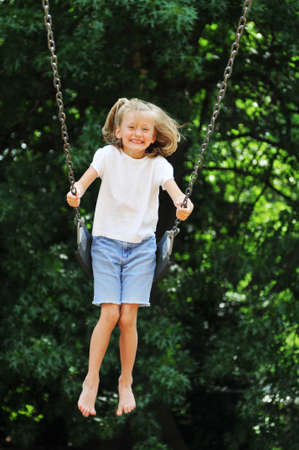 Little girl swinging on a sunny day with trees in the background Stock Photo