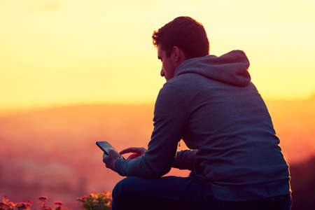sad lonely: Young man with phone at the sunrise. Stock Photo