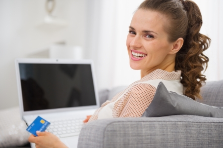 smiling young housewife with laptop and credit card sitting on