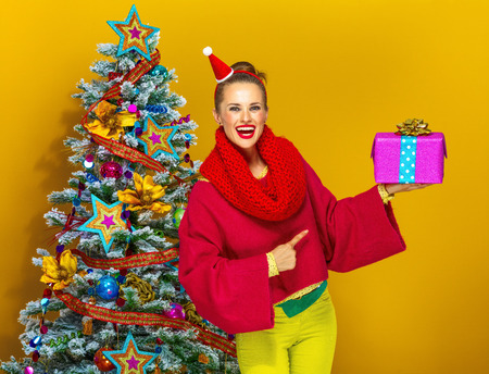 お祭りの季節 クリスマス ツリー クリスマス プレゼント ボックスを指して黄色の背景上に孤立に近いカラフルな服装で幸せな若い女 の写真素材 画像素材 Image