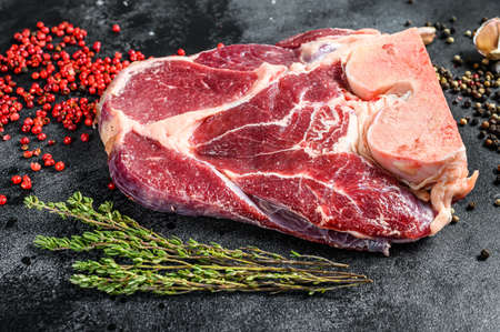 Raw beef shank with spices and herbs. Black background. Top view.