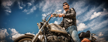 Biker man wearing a leather jacket and sunglasses sitting on his motorcycle. Фото со стока