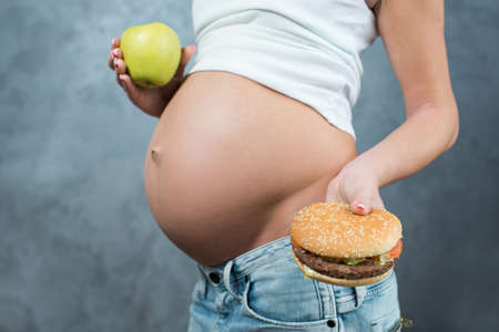 かわいい妊婦腹とジャンク フードのクローズ アップ ハンバーガーとポテトと妊娠 妊娠中の女性の不健康な母性の概念 妊娠中の腹ボディ部側面図 の写真素材 画像素材 Image