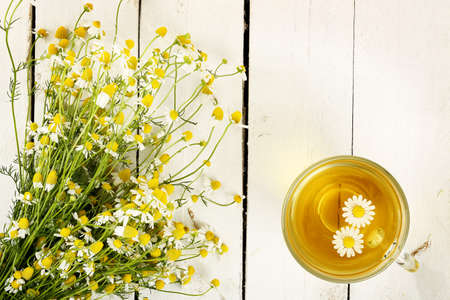 cup of chamomile tea with chamomile flowers on white wooden planks - 39909233