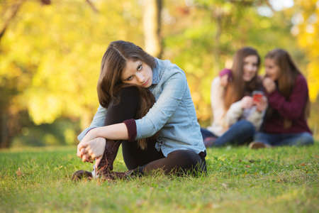 Lonely girl leaning on knee in front of teenagers talking - 37424342