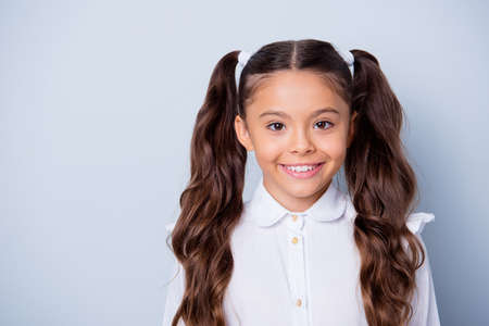 First grade schoolkid. portrait of nice cute cheerful positive latin ethnicity girl with curly pigtails in white formal shirt. copy-space, isolated over grey background