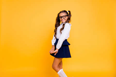 Profile side view portrait of nice, lovely, sweet, adorable, beautiful small girl isolated on shine yellow background stands half a turn and looks into the camera