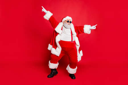 Full body photo of funky fat santa claus with big funny abdomen dancing raising arms wearing style stylish trendy eyewear eyeglasses isolated over red background