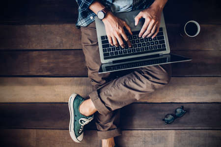 Businessman sitting on wooden floor with coffee cup and glasses using laptop working at home to send and send reply to email message customer service