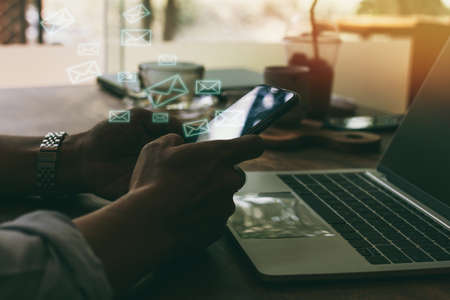 Newsletter concept hand of asian man checking message box on digital mobile phone with laptop the table at coffee shop Stock Photo