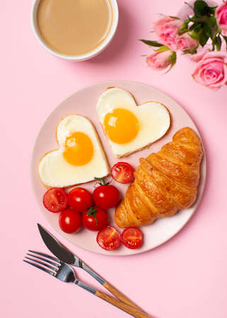 Petit déjeuner sain de vacances avec des coeurs d'oeufs et une tasse de café, fleurs roses sur fond rose, vue de dessus, espace de copie, vertical Banque d'images