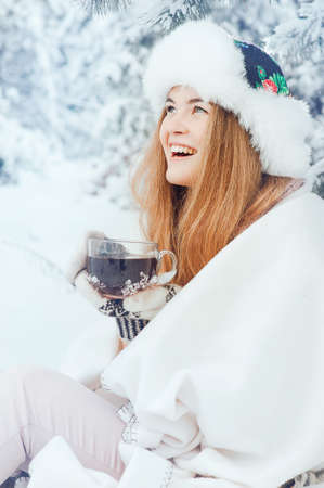 Beautiful girl smiling with a cup of coffee on the background winter forest