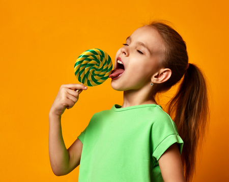 Happy young little child girl kid bite sweet lollypop candy on yellow background - 94363294