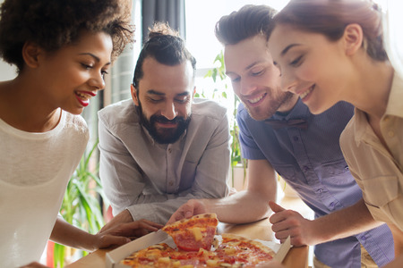 Geschäft, Lebensmittel, Mittagessen und Leutekonzept - glückliches Geschäftsteam, das Pizza im Büro isst Foto auf Lager