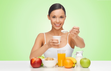 people, healthy food, diet and weight loss concept - happy beautiful woman with fruits eating yogurt for breakfast over green background - 50455926