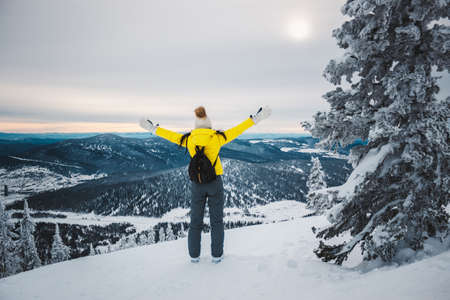 黄色のジャケット 白い帽子と黒いバックパックを背負って立つ若い女の子モミの木 山の頂上に近く背中太陽の手に達するし 雪に覆われた谷を見て の写真素材 画像素材 Image
