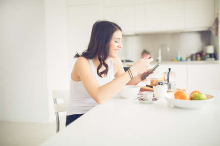 Jeune brune est en train de lire le journal tout en prenant le petit déjeuner à la maison. Femme moderne mode de vie sain-sain petit-déjeuner, café et fruits, lire des citations de motivation. Commencez votre journée, énergie positive Photo