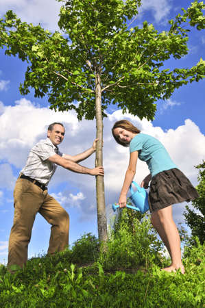 Father and daughter watering a young tree Фото со стока