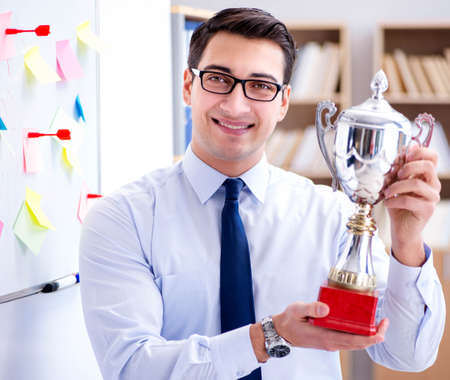 Young businessman receiving prize cup in office