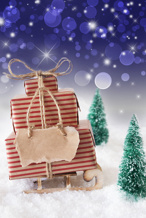 そりやクリスマス ギフトやプレゼントとそり 雪と木と雪の風景 紫色の輝く背景ボケ効果を持つ 広告またはフリー テキストのコピー スペース ラベル 垂直方向の画像 の写真素材 画像素材 Image