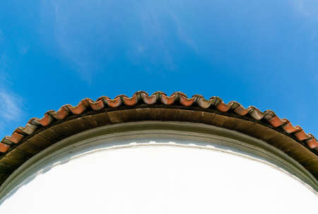View from below of the edge of a circular tile roof over blue sky