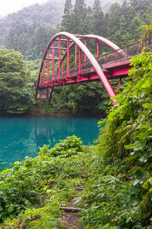 Forest Lake Shore With Path And Red Suspension Bridge. Japanese