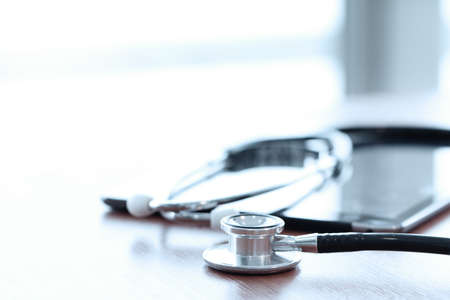 Stethoscope with digital tablet computer on wooden table and background