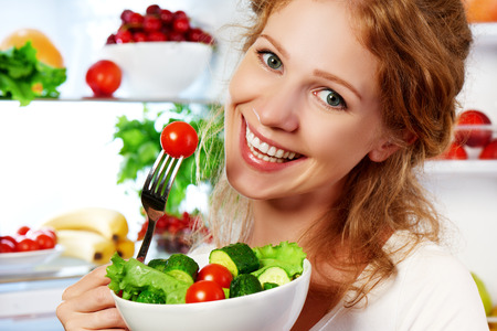 femme heureuse mange des aliments sains légumes salade végétarienne sur réfrigérateur Photo stock